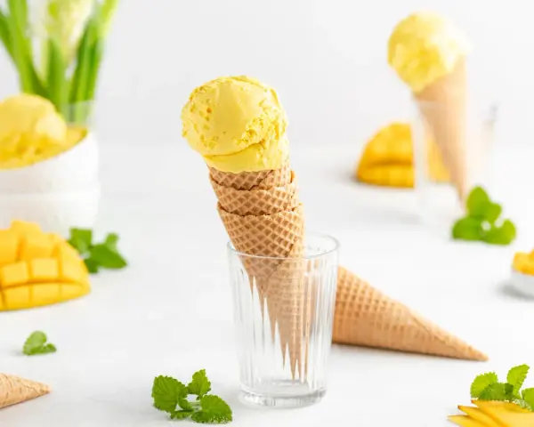 Ein Stapel Waffelkegel mit cremigem Mango Eis, garniert mit frischer Minze und Mangostücken. Ein süßer Genuss!