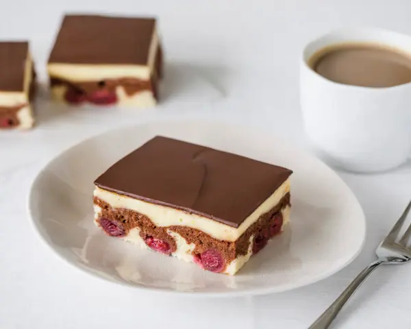 Ein Stück Donauwelle-Kuchen mit Kirschen, Vanillecreme und Schokoladenglasur. Ein leckeres Rezept für den Kaffeetisch.