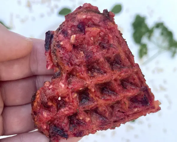 Herzhafte Waffeln aus Roter Bete, gehalten von einer Hand. Ein gesunder Snack mit leckerer Textur.