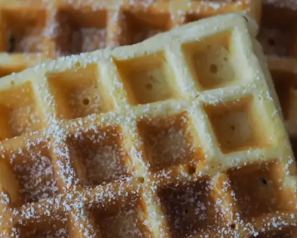 Goldbraune Waffeln, bestäubt mit Puderzucker, warten auf Joghurt. Ein süßer Genuss!