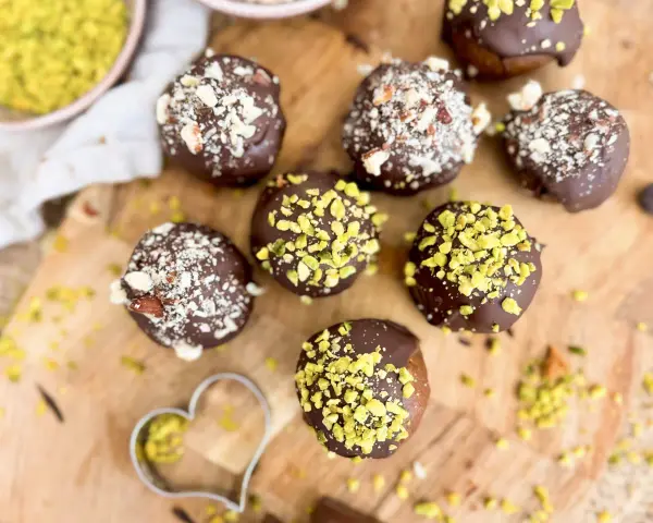 Selbstgemachte Pralinen mit Schokolade und gehackten Nüssen, einige mit Pistazien bestreut. Ein Herz-Ausstecher liegt daneben.