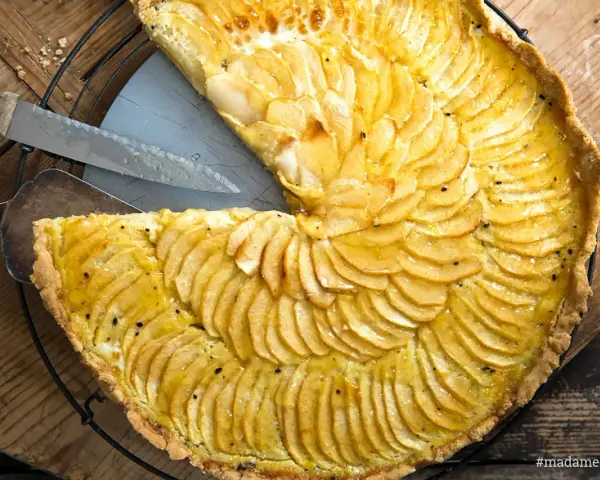 Ein köstliches Apfeltarte Rezept mit dünn geschnittenen Äpfeln, die wie Fächer angeordnet sind. Ein Stück wurde bereits herausgeschnitten.