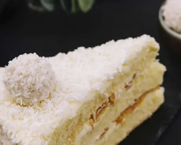 Ein Stück Raffaello Torte, bedeckt mit Kokosraspeln und einer Raffaello-Kugel.
