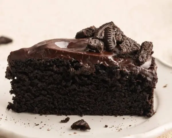 Ein saftiges Stück dunkler Oreo Kuchen mit glänzender Schokoladenglasur und zerbröselten Keksen obendrauf.