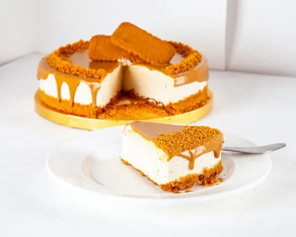 Ein cremiger Lotus Cheesecake mit Karamellglasuren und Keksbröseln. Ein Stück auf einem Teller, daneben ein ganzer Kuchen.