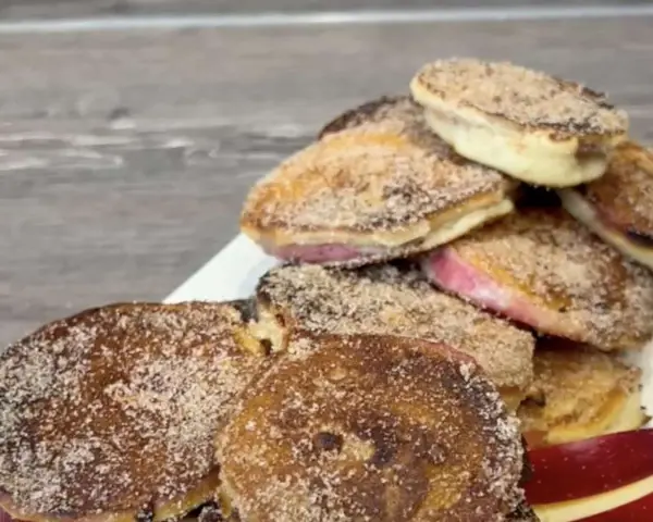 Ein Haufen goldbrauner, mit Zimt und Zucker bestreuter Apfelküchlein, die köstlich aussehen.