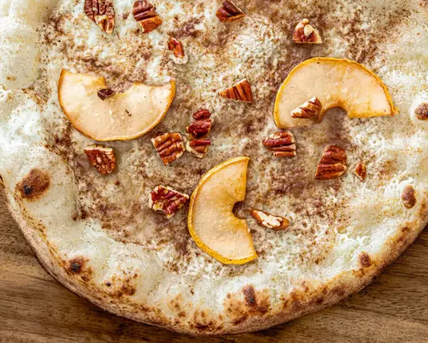Eine süße Pizza mit dünnem Teig, bestreut mit Zimt, belegt mit Apfelscheiben und Pekannüssen. Ein Genuss wie eine Nutella Pizza!