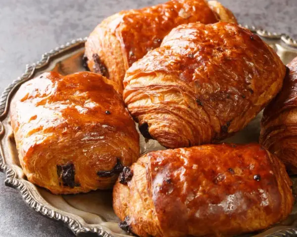 Einige goldbraune, knusprige Pain au Chocolat liegen auf einer silbernen Platte.