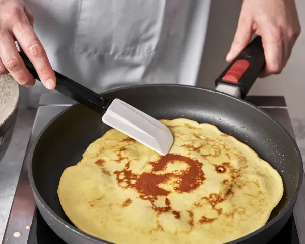 Ein goldbrauner Quark Pfannkuchen wird in einer Pfanne mit einem Spatel gewendet.