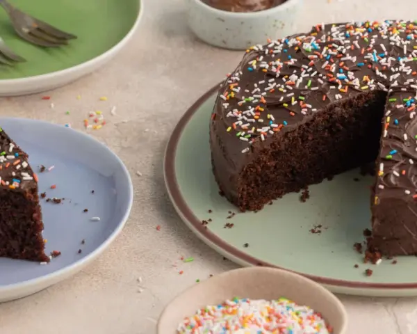Ein saftiger Nutella Kuchen mit Schokoladenglasur und bunten Streuseln, ein Stück auf einem Teller, bereit zum Genießen.