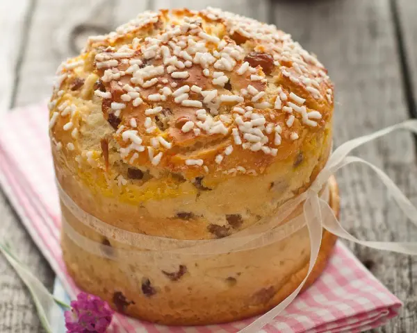 Ein goldbrauner Panettone mit Rosinen und Zuckerkristallen, gebunden mit einem Satinband. Ein köstliches Panettone Rezept zum Nachbacken.
