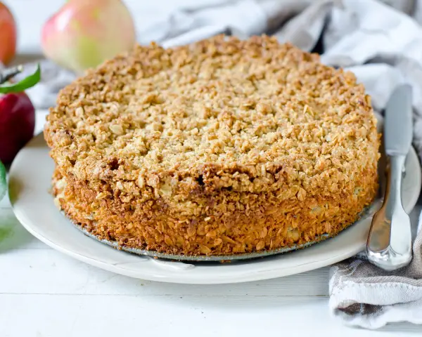 Ein goldbrauner Haferflocken Kuchen mit knuspriger Kruste, daneben Äpfel und ein Messer.