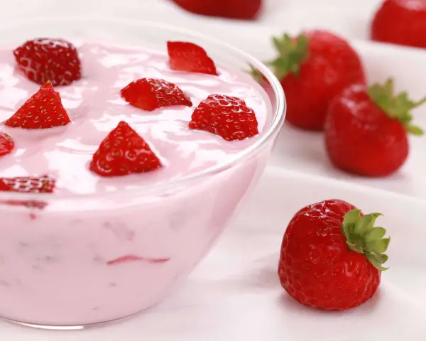 Ein cremiges Erdbeer Dessert in einer Schüssel, garniert mit frischen Erdbeerstücken. Daneben liegen ganze Erdbeeren.