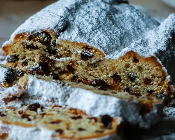 Ein saftiger Stollen, bestäubt mit Puderzucker, zeigt sein Inneres voller Rosinen. Ein köstliches Stollen Rezept zum Nachbacken.