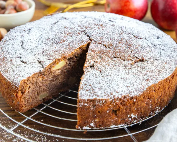 Ein saftiger russischer Apfelkuchen, bestäubt mit Puderzucker, wartet auf seine Genießer. Apfelstücke sind im dunklen Teig sichtbar.