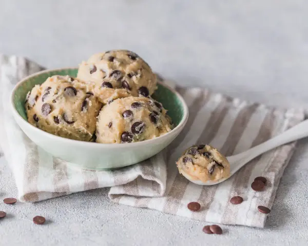 Schüssel mit Kugeln von Cookie Dough Rezept, Löffel mit Teig und Schokostückchen.