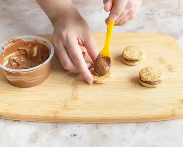 Hände belegen Kekse mit Nutella. Leckere Nutella Kekse entstehen auf dem Holzbrett.