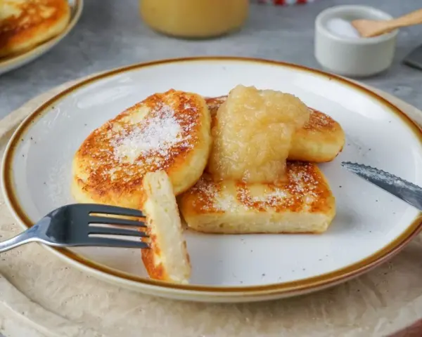 Goldbraune Quarkkeulchen, bestreut mit Puderzucker, serviert mit Apfelmus. Ein köstliches Quarkkeulchen Rezept zum Genießen.
