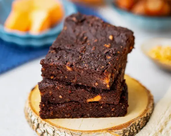 Gestapelte, saftige vegane Brownies mit Nüssen, auf einem Holzscheit.