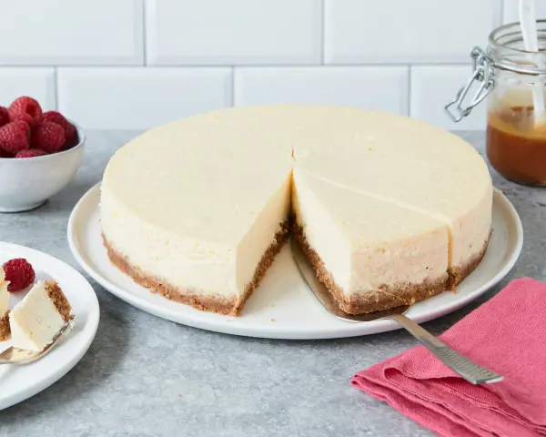 Ein cremiger New York Cheesecake mit knusprigem Boden, garniert mit Himbeeren und Karamell.