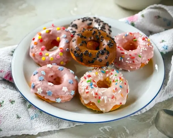 Sechs bunte Donuts auf einem Teller, perfekt für ein schnelles Donuts Rezept. Mit Streuseln und Sternen verziert.