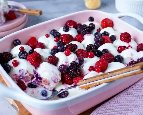 Ein cremiges Windbeutel-Dessert mit frischen Beeren wie Himbeeren, Brombeeren und Blaubeeren, serviert in einer rosa Schale.