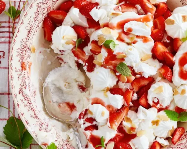 Ein köstlicher Eton Mess mit frischen Erdbeeren, Baiser und Sahne, garniert mit Mandelsplittern und Minze.