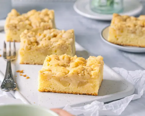 Saftiger Apfelkuchen mit Streuseln, perfekt für eine Kaffeepause. Ein Stück ist schon auf einer kleinen Platte angerichtet.