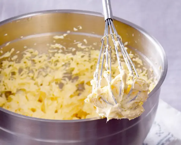 Ein Schneebesen mit cremigem Teig, bereit für ein Buttercreme Rezept.