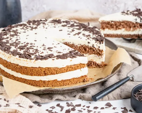 Eine köstliche Cappuccino Torte mit Schokoladenraspeln bestreut, auf einem Teller mit einem angeschnittenen Stück.