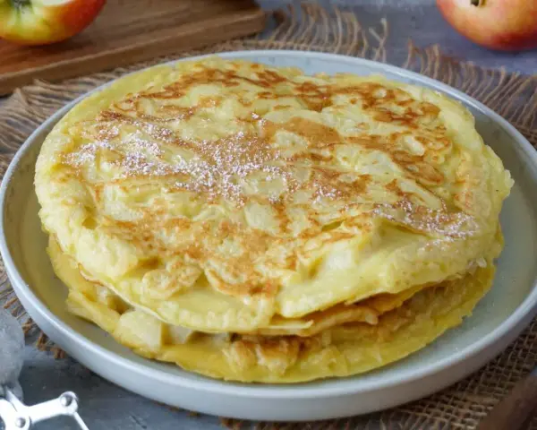 Ein Stapel goldbrauner Apfelpfannkuchen, bestäubt mit Puderzucker. Ein köstliches Apfelpfannkuchen Rezept für jeden Anlass.