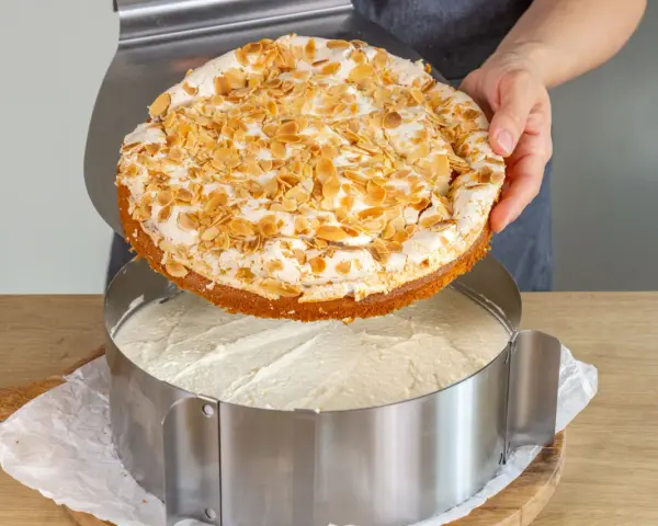 Eine köstliche Stachelbeer Baiser Torte mit Mandel-Topping wird gerade in einen Tortenring gesetzt.