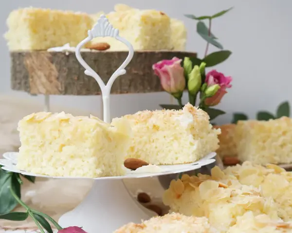 Saftige Buttermilchkuchenstücke mit Mandelsplittern und Kokosraspeln, garniert mit Blumen.