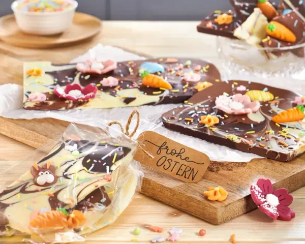 Bruchschokolade selber machen: Bunte Oster-Schokoladentafeln mit Karotten, Blumen und Streuseln, verpackt und mit "Frohe Ostern"-Anhänger.