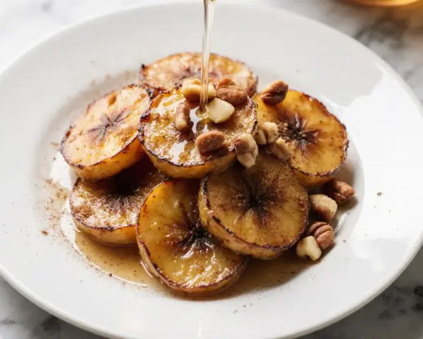 Gebackene Banane mit Nüssen und Sirup beträufelt, ein süßer Genuss auf einem weißen Teller.