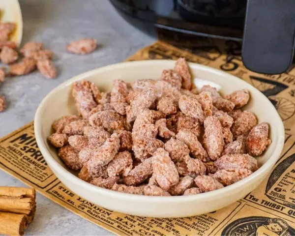 Schüssel voller gebrannter Mandeln, perfekt für ein schnelles gebrannte mandeln rezept. Zimtstangen liegen daneben.