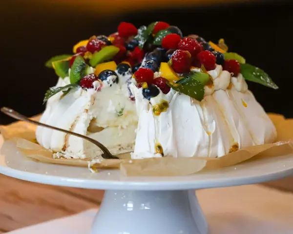Ein köstliches Pavlova-Rezept mit frischen Beeren, Kiwi und Passionsfrucht. Ein Stück ist bereits angeschnitten.