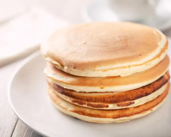 Ein Stapel goldbrauner, glutenfreier Pfannkuchen auf einem weißen Teller, bereit zum Genießen.