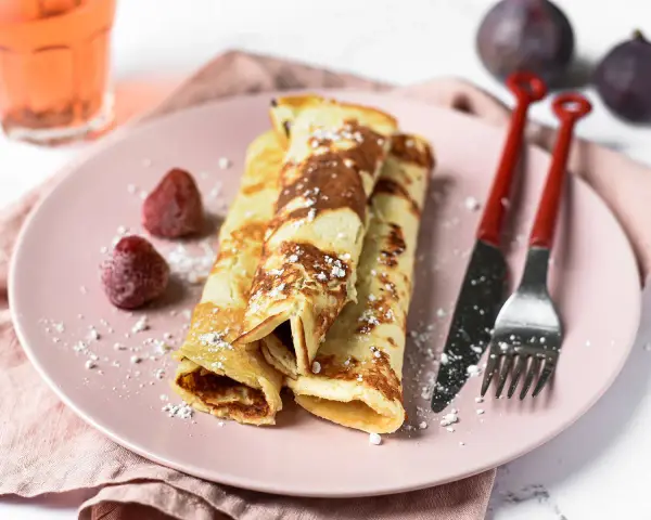 Gefüllte Pfannkuchen ohne Mehl, bestäubt mit Puderzucker, serviert mit Erdbeeren und Feigen.