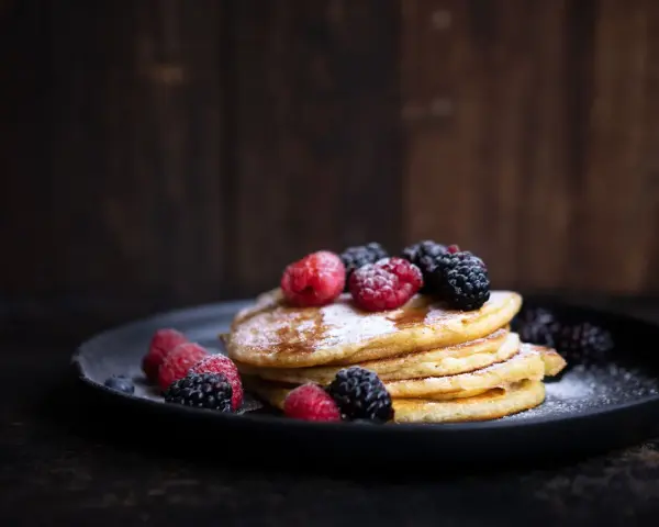 Stapel goldbrauner Pancakes, bestäubt mit Puderzucker und garniert mit frischen Himbeeren und Brombeeren. Ein köstliches Pancakes Rezept für jeden Anlass.
