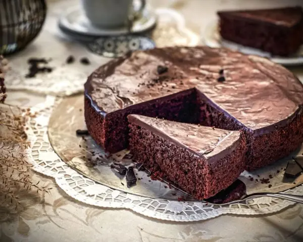 Ein saftiger, schneller Schokokuchen mit glänzender Glasur und einer Kuchenscheibe auf einem Tortenheber.