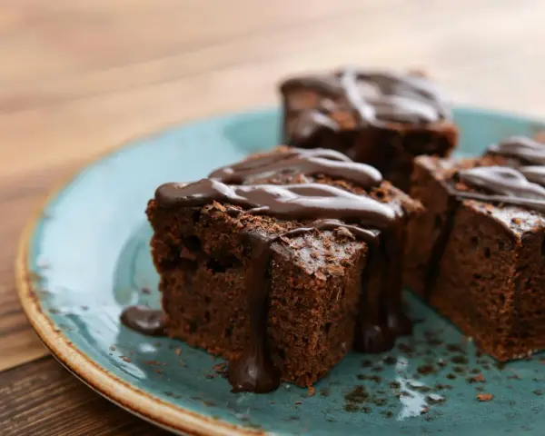 Saftige Brownies, perfekt für ein schnelles Brownie Rezept. Mit flüssiger Schokolade übergossen und auf einem türkisfarbenen Teller angerichtet.