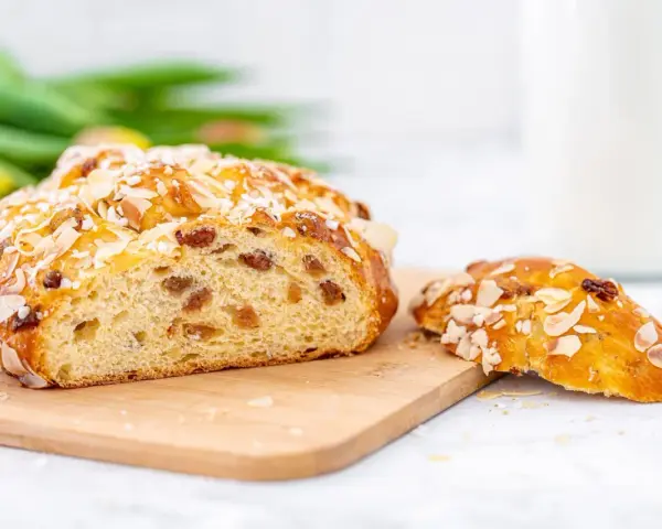 Ein goldbraunes Osterbrot mit Mandelsplittern und Rosinen, perfekt für Ihr Osterbrot Rezept. Daneben ein Stück des süßen Gebäcks.