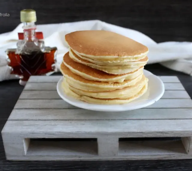 Ein Stapel goldbrauner Pfannkuchen, bereit für ein köstliches Frühstück. Daneben eine kleine Flasche Ahornsirup. Ein einfaches Pfannkuchen Rezept für jeden Tag.