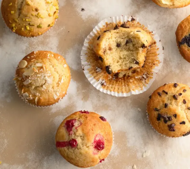Verschiedene Muffins, perfekt für ein schnelles Muffins Rezept: Schoko, Blaubeer, Himbeer und Pistazien. Ein Bissen fehlt vom Schokomuffin.