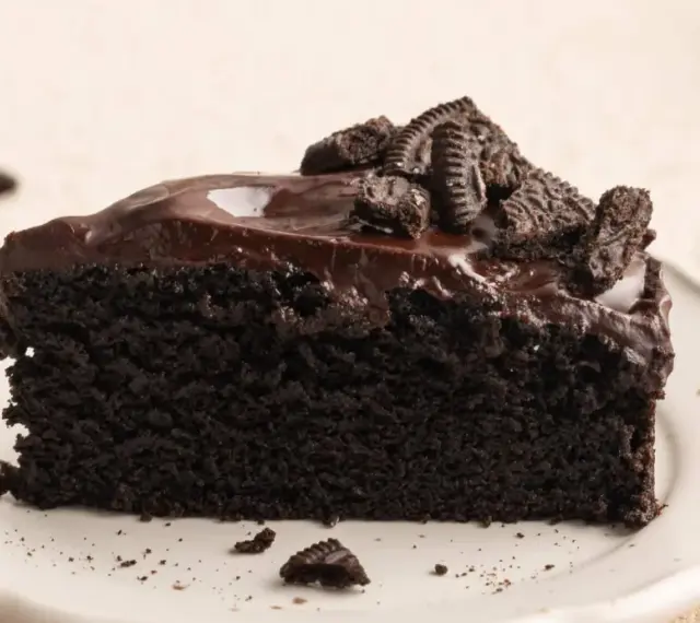 Ein saftiges Stück dunkler Oreo Kuchen mit glänzender Schokoladenglasur und zerbröselten Keksen obendrauf.