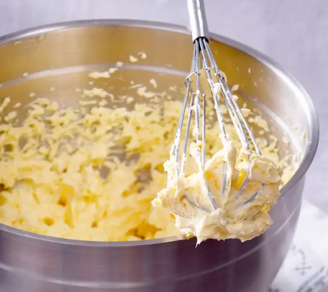 Ein Schneebesen mit cremigem Teig, bereit für ein Buttercreme Rezept.