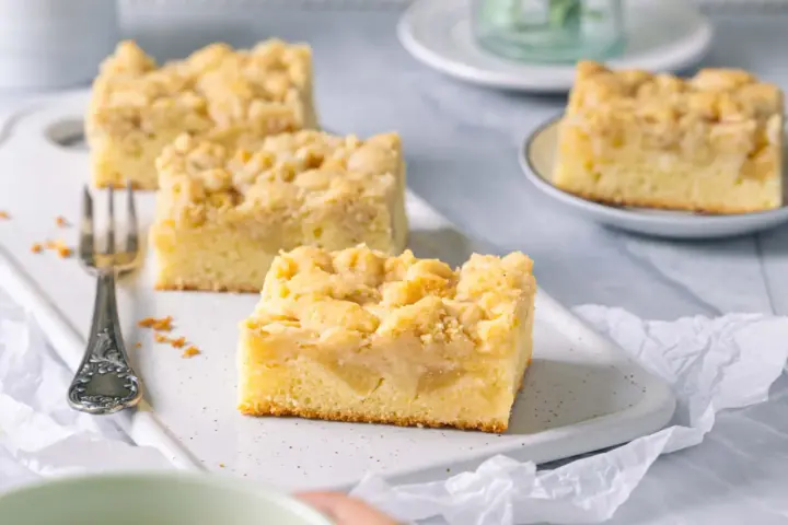 Saftiger Apfelkuchen mit Streuseln, perfekt für eine Kaffeepause. Ein Stück ist schon auf einer kleinen Platte angerichtet.