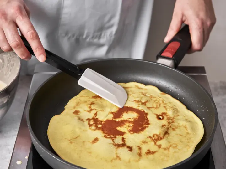 Ein goldbrauner Quark Pfannkuchen wird in einer Pfanne mit einem Spatel gewendet.
