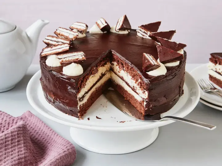 Eine köstliche Kinder Pingui Torte mit Schokoladenglasur, Sahnetupfern und kleinen Schoko-Biskuit-Stücken. Ein Stück ist bereits angeschnitten.